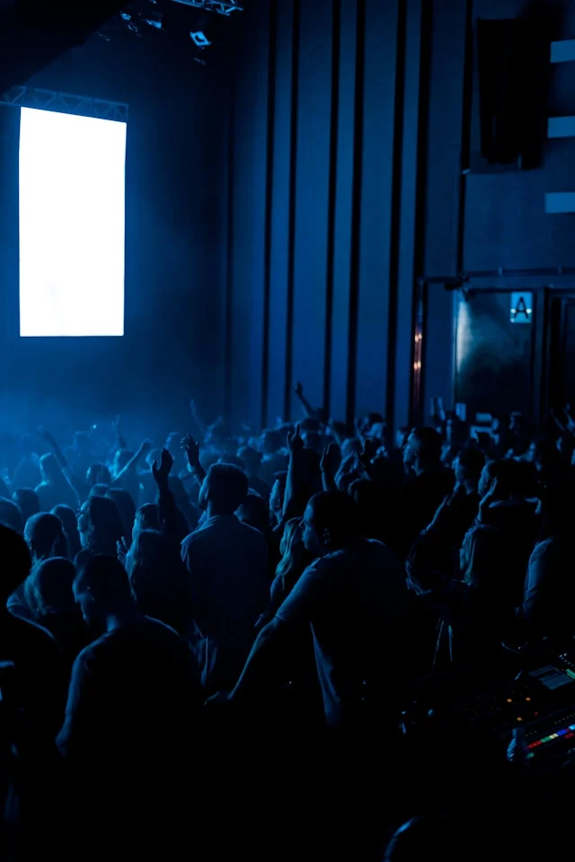 Audience at a corporate conference or keynote in a dimly lit auditorium facing a large presentation screen.